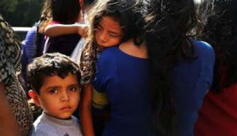 A concerned child looks on as others embrace, capturing a moment of vulnerability and connection during a poignant scene.