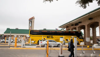 Yellow NTX Charters bus at a transportation hub, with a person walking by and a cloudy sky overhead.